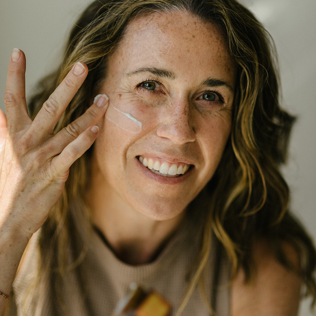 Confident woman applying Solterra Tallow Balm to her cheek, embracing fine lines and natural radiance in a pro-aging skincare ritual