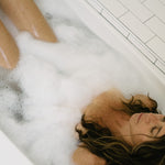 Peaceful woman soaking in a bubble-filled bathtub, eyes closed in relaxation, highlighting a serene self-care moment in a tiled bathroom